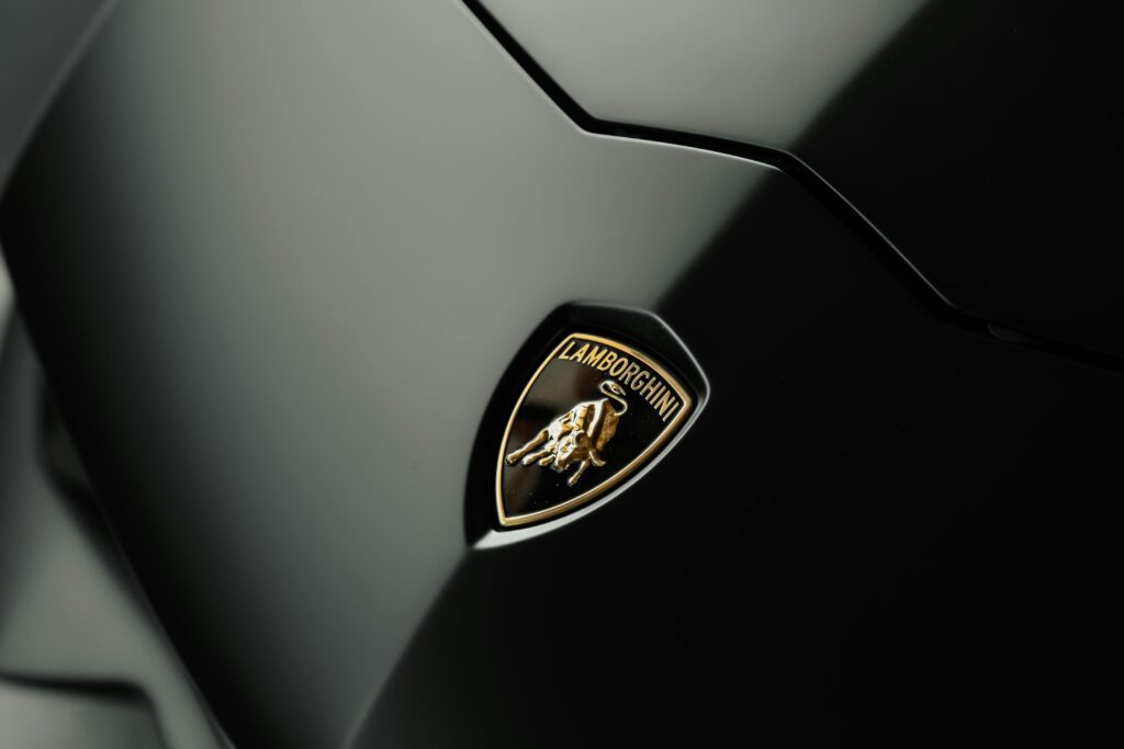 Detailed close-up photo of a Lamborghini logo on a sleek black car hood, symbolizing luxury and style.